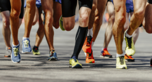 Eine Gruppe von Läufern in Sportschuhen und -kleidung rennt auf einer gepflasterten Straße, wobei nur ihre Beine und Füße zu sehen sind, während sie sich dicht nebeneinander vorwärts bewegen.